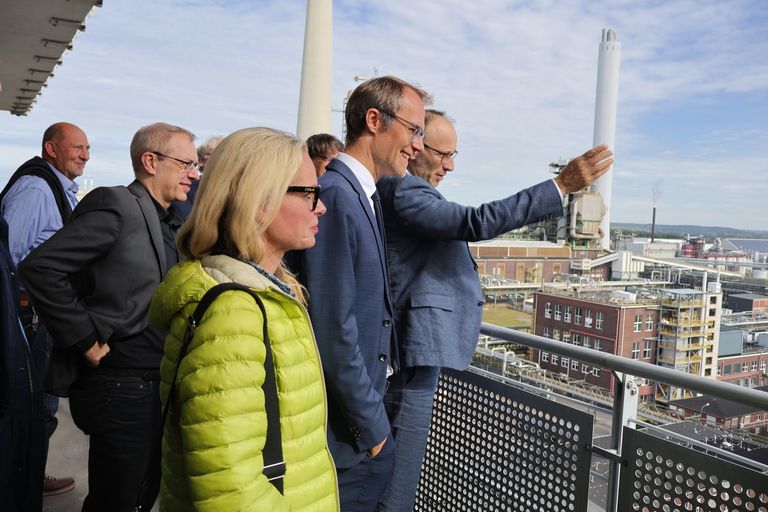 Gruppe von Menschen auf Aussichtsplattform mit Blick über Stadt, einer zeigt nach oben.